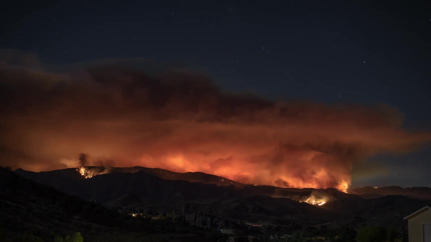 A raging fire blazes across mountains in the night sky