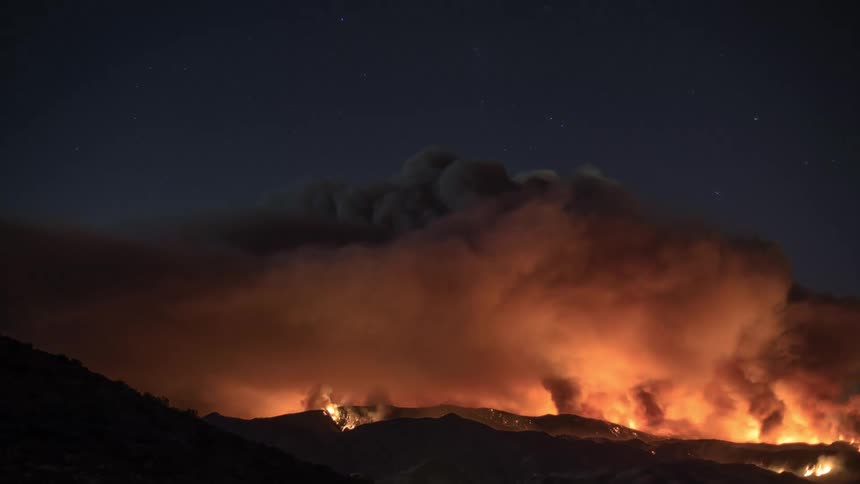 A raging fire blazes across mountains as smoke fills the night sky