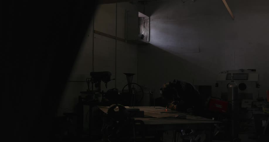 Sparks flying around a welder in a dark workshop