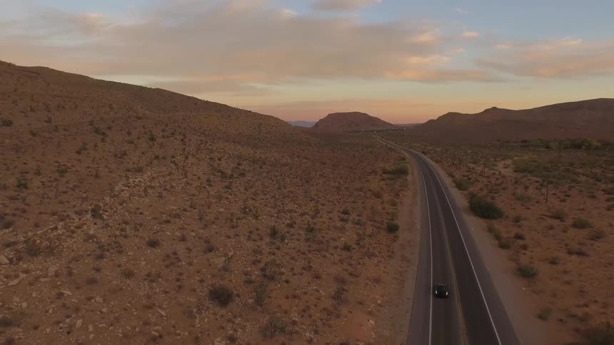 Vehicle drives on a road in the desert at sunset