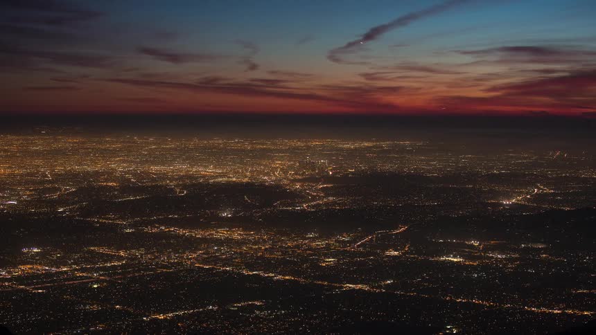 The lights in a big city shine and twinkle as traffic moves across town and buildings are lit up and a red sky turns to darkness and the lights get brighter