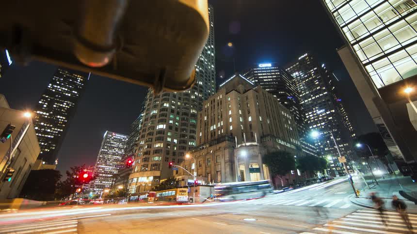 Lights on tall city buildings are lit up in the darkness as traffic moves on the streets and pedestrians are walking