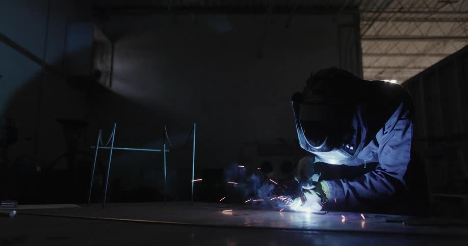 A welder leaning over using a torch causing sparks and smoke in the dark