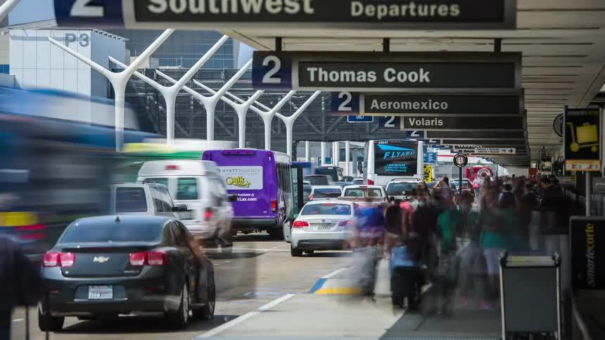 A fast-paced hyperlapse shot of a busy airport showing travelers loading and unloading baggage outside a busy terminal