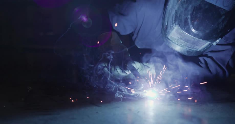 Sparks flying around a welder in a dark workshop