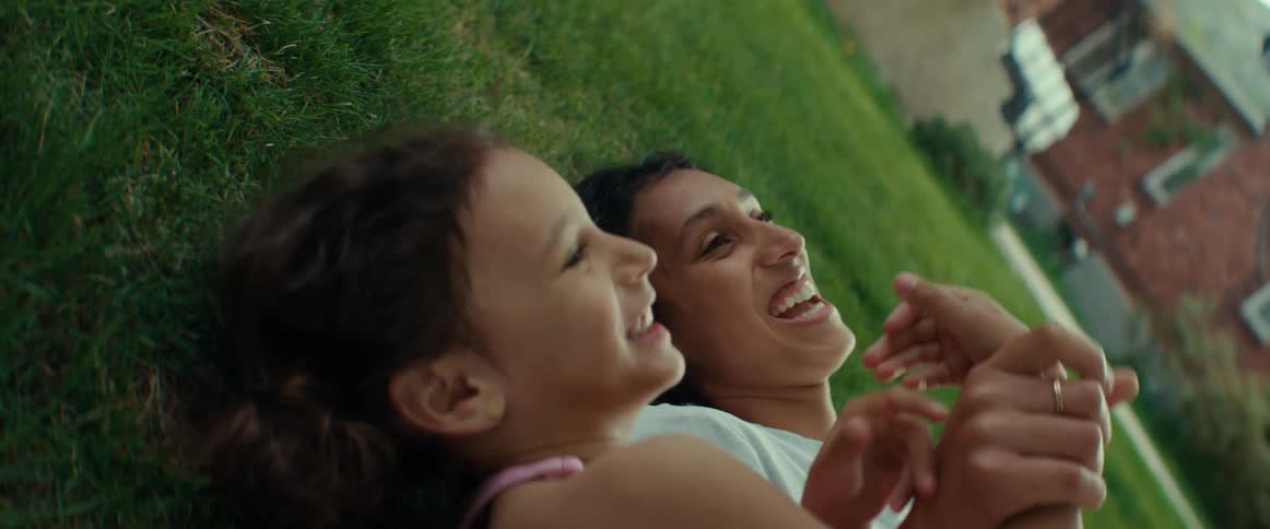 A mom and daughter lying in the grass talking laughing and holding hands