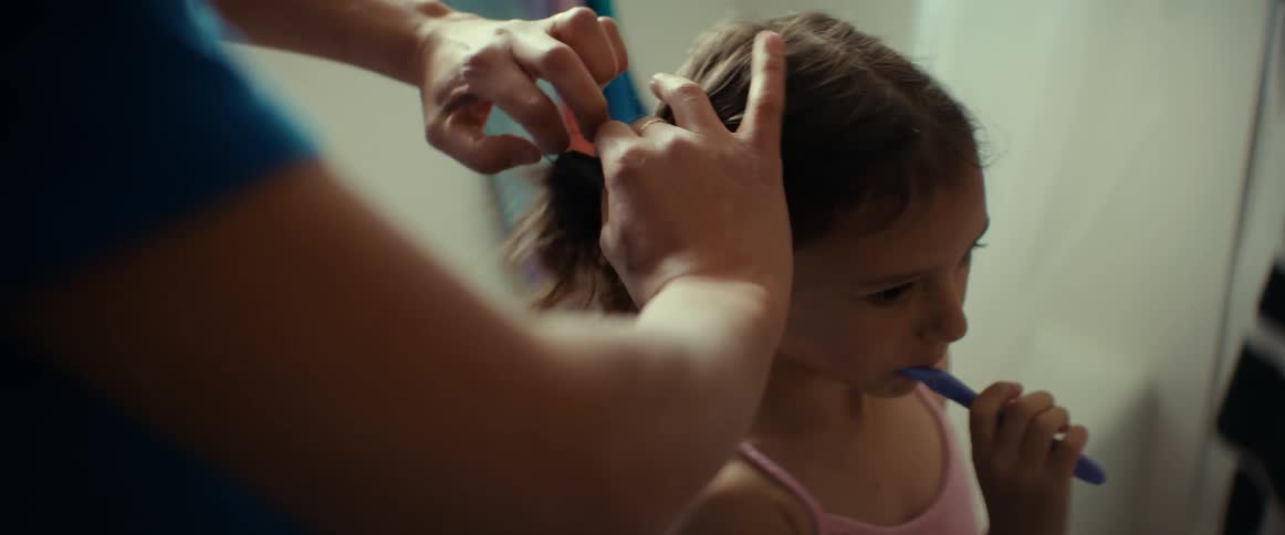 A mother putting her young daughters hair in pigtails while brushing teeth