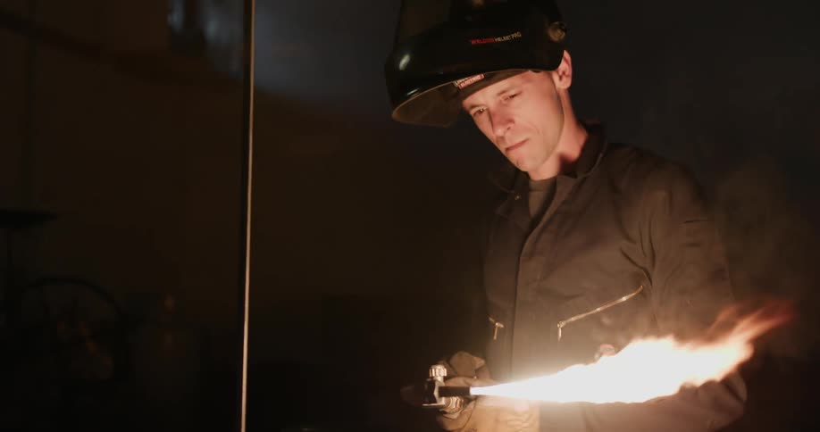A man lights a welding torch then drops his helmet visor once the flame is going