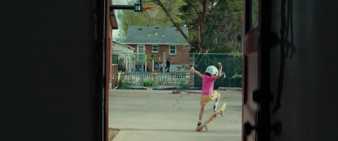 A young girl in a helmet jumping on a skateboard outside on a summer day