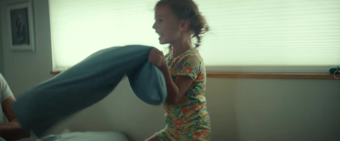 Mother and daughter smile during pillow fight in bedroom