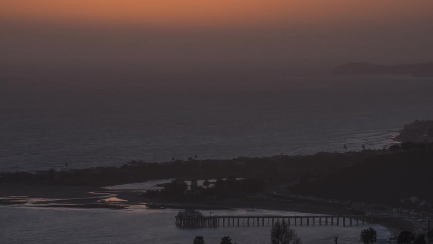 The sun sets over a pier along the coast