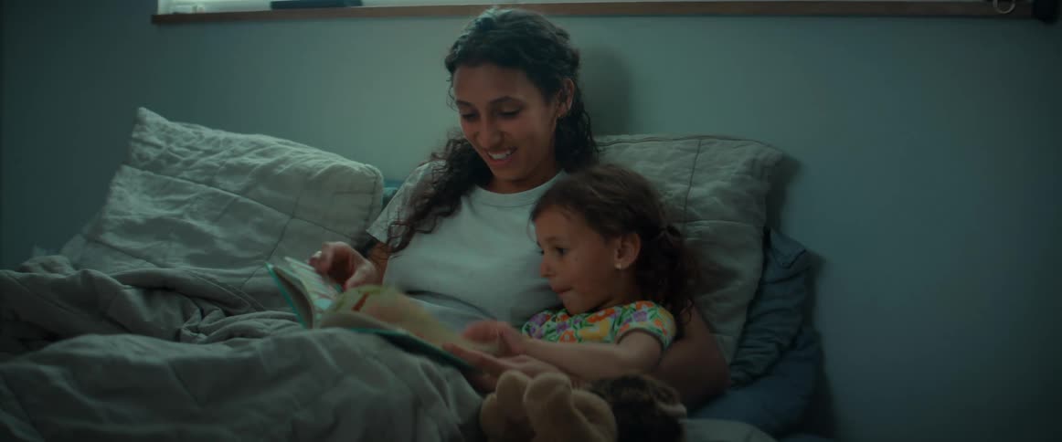 A mother and daughter read a book together as they lay in bed
