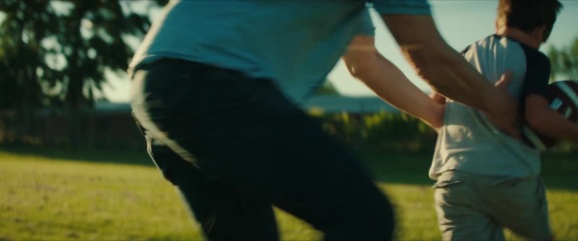 A dad is in a park with his son playing football on the grass
