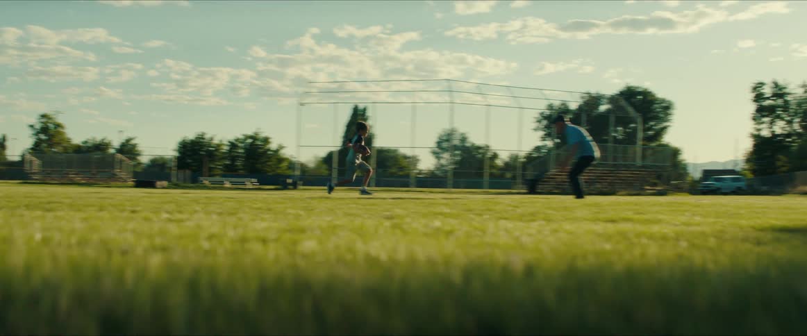 A little boy carrying a football tries to get past his dad while they play at the park