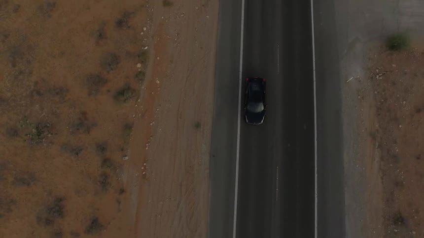 A black car travels down a road by the desert