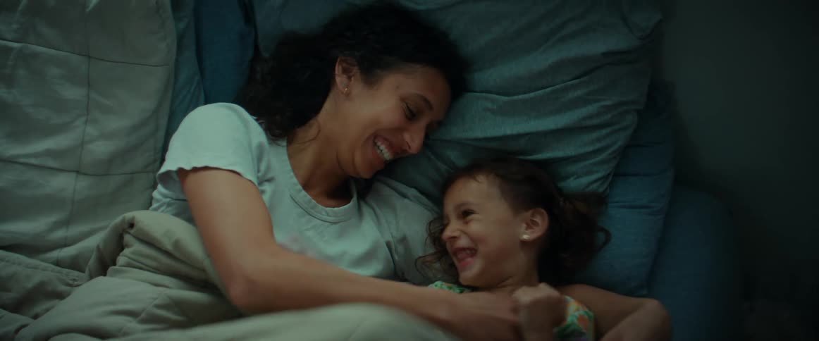 Mother tickles daughter then hugs her as they lie in bed