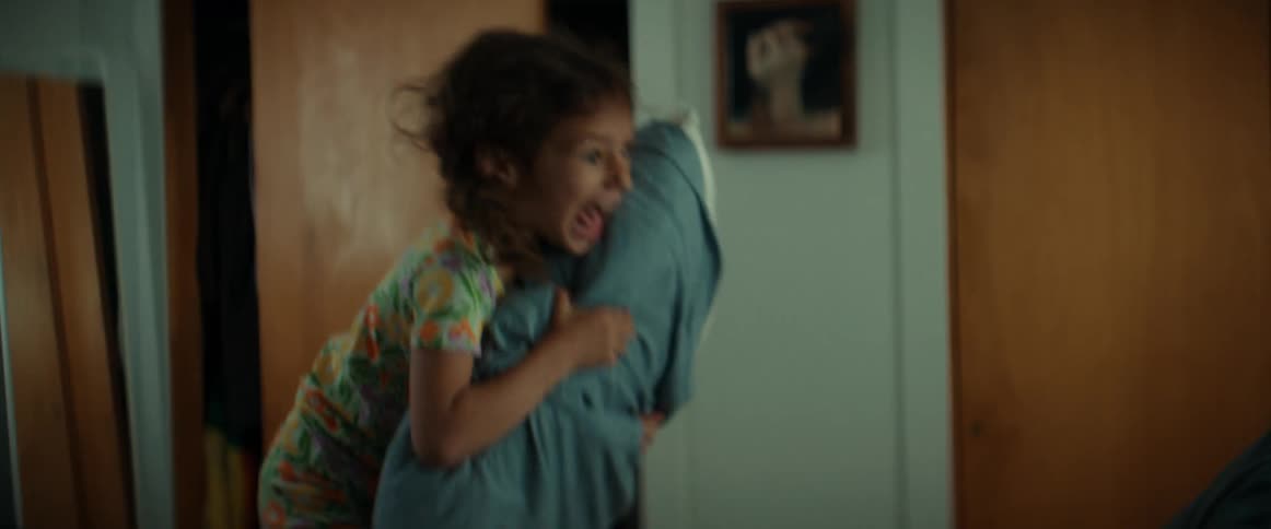 A girl holding a pillow yells as she jumps onto her mom on the bed both laughing