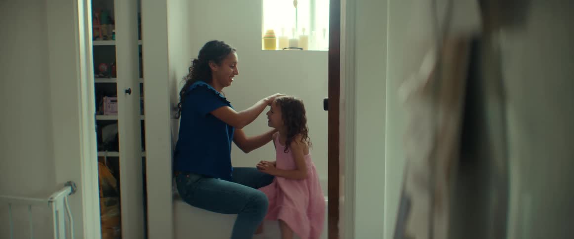 A woman is sitting in the bathroom fixing her young daughters hair