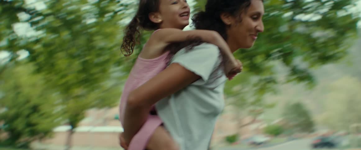 A little girl rides piggy back on her mom as they spin and run around the yard