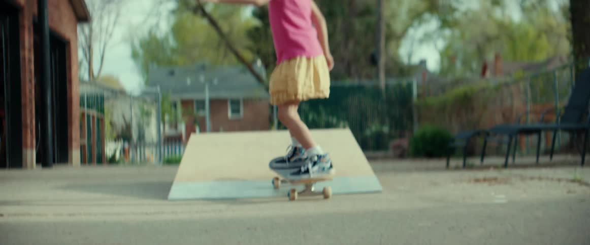 Girl wearing helmet rides skateboard up and down ramp in driveway