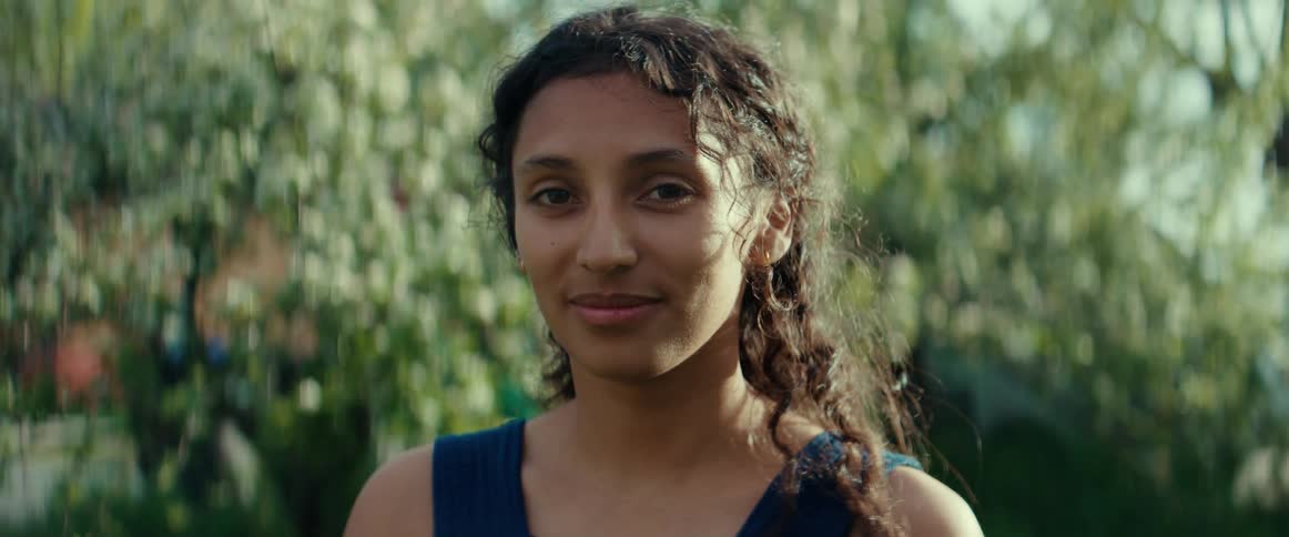 A young woman standing outside near trees as her hair moves in the breeze