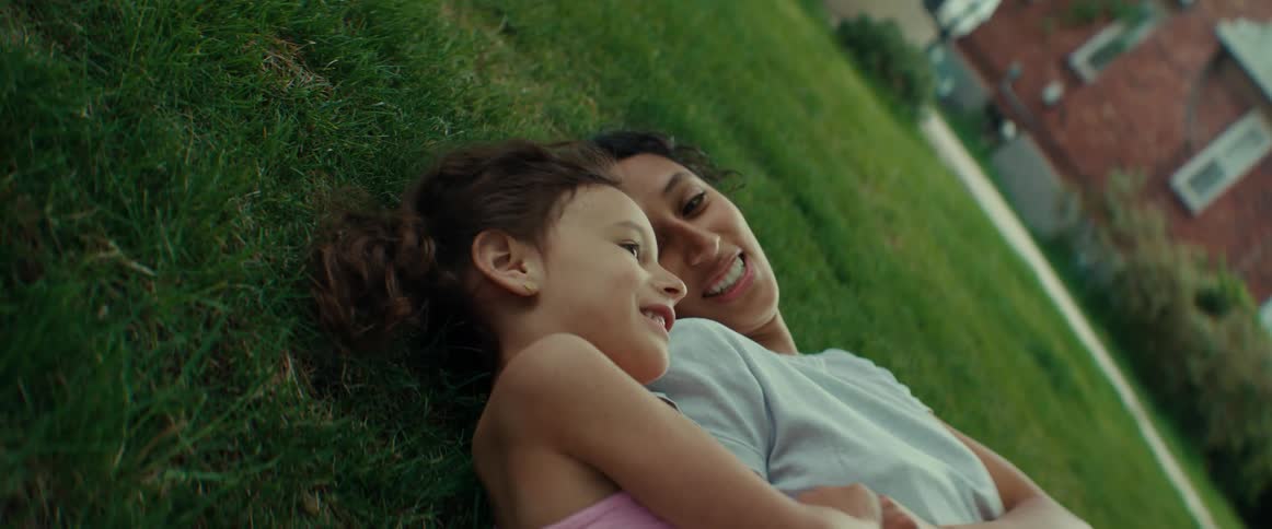 Mother and daughter lie on lawn smiling and talking