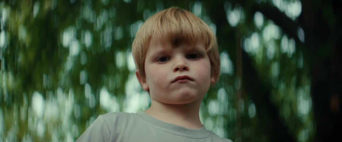 A young boy is standing outside near a tree looking unhappy