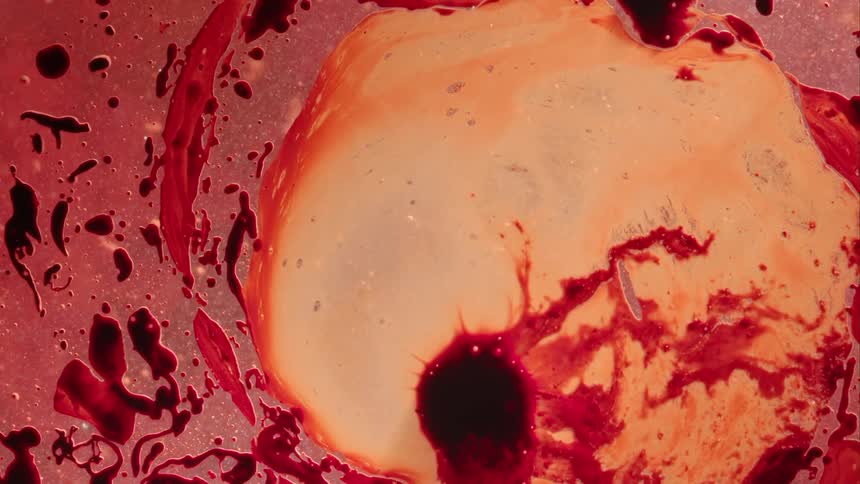 A red bubble erupts in a liquid like substance and spreads out inside the bubble and the outside shapes move as it grows