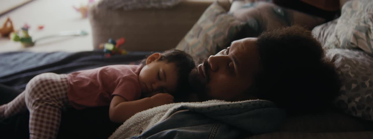 A man is sleeping on a couch with his baby sleeping on his chest
