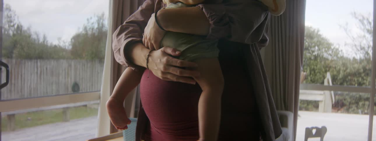 A pregnant woman holds her squirming toddler in her arms against her belly