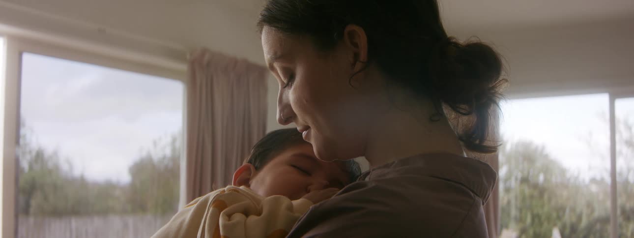 Mother cuddles thumb sucking child against her chest and rocks them