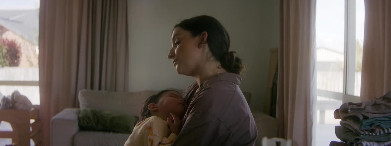 A woman rocks a young sleeping child in her arms while sitting in the living room of a house during the day