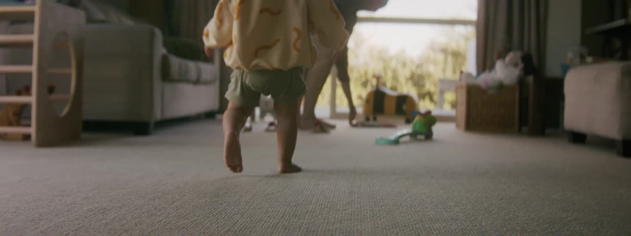 A toddler is walking inside by there parent in the daytime
