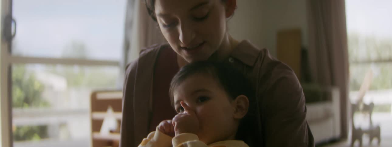 Happy mother sitting on the floor with her son on her lap while the baby is sucking his thumb