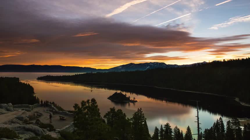 People walk around near a lake at sunset