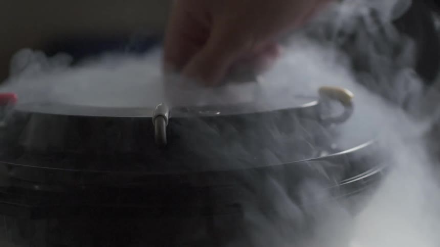 A person dips a rod into a steaming cylinder