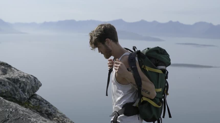 Active male hiker taking off his gear while walking along a rugged mountain ridge.