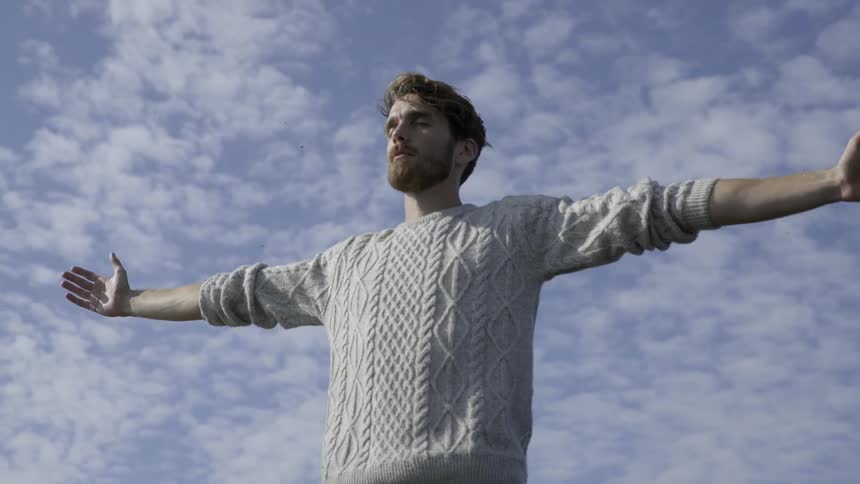 A man holds his arms outstretched while standing on a high rocky mountain peak.