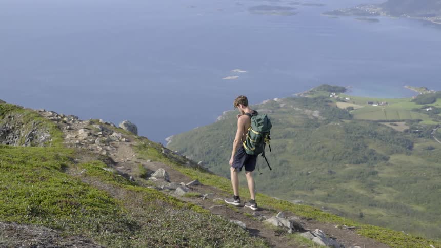 Adventurous male hiker climbing a rugged mountain ridge with scenic natural views in summer.
