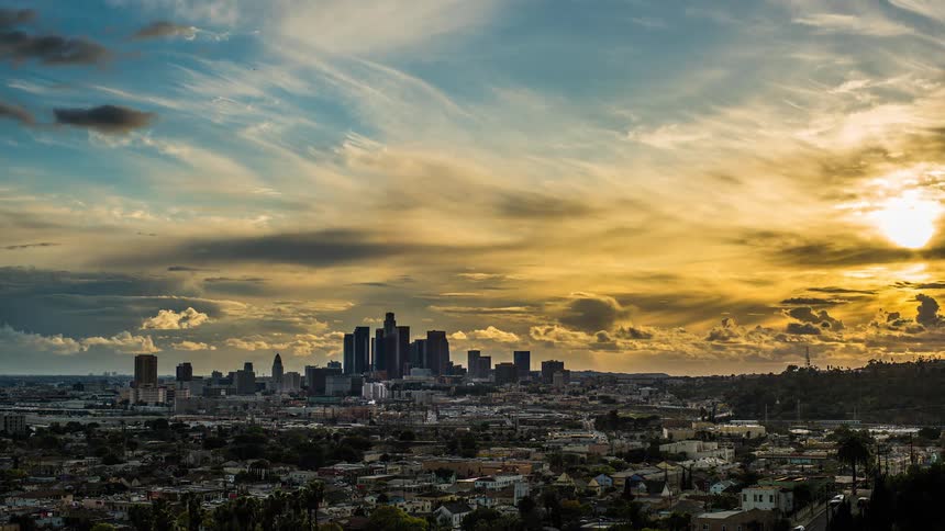 Rain clouds move across the sky over a city as the sun sets into evening