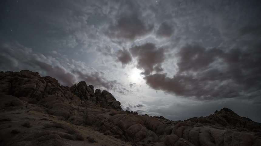 Clouds move over the sky above mountains as the moon shines brightly