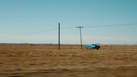 A retro car travels along a road through the countryside on a clear day