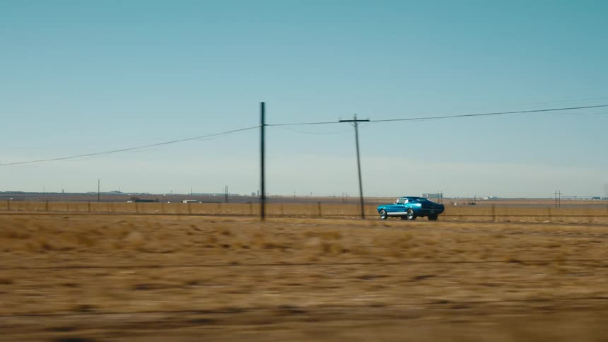 A retro car travels along a road through the countryside on a clear day