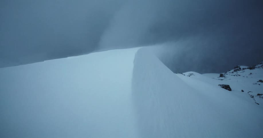 Snow blows from a snow drift near the rocks at night