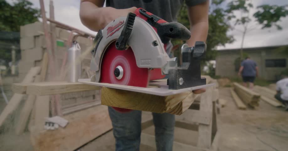 Worker cuts wooden board using power saw on construction site