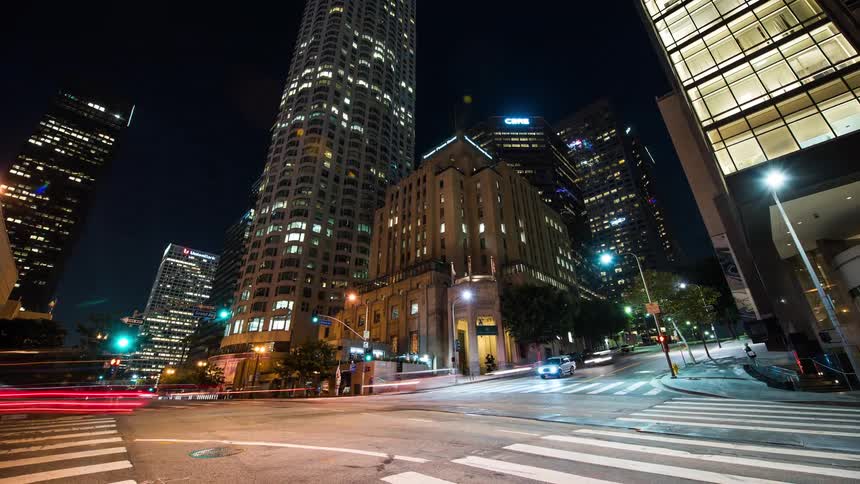 Traffic travels through the city intersection at night while pedestrians cross in the crosswalk