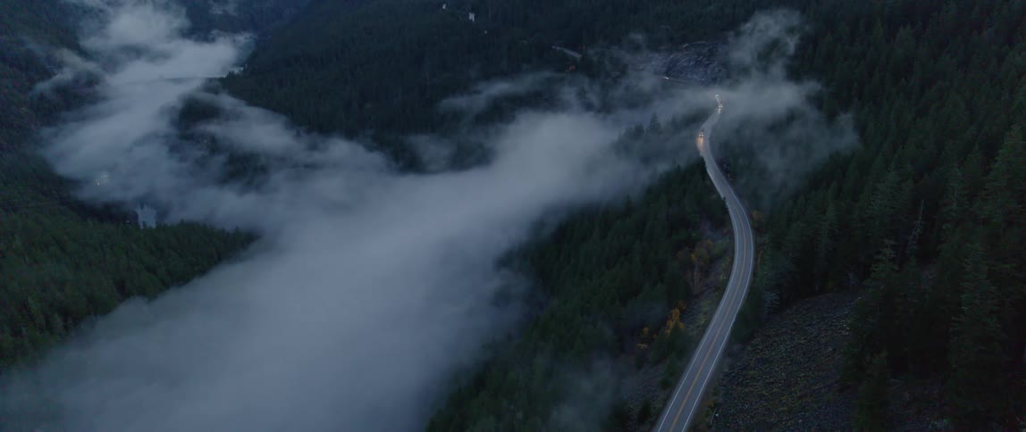 Vehicle headlights shine through fog on highway mountain slope