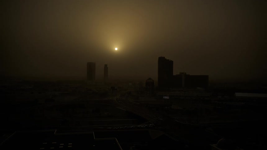 A time lapse of the sun setting over a city skyline as cars drive on streets in dust storm