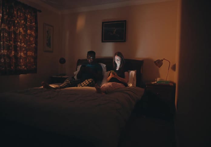 Man and woman lay in bed in a dark bedroom and look at their cellphones