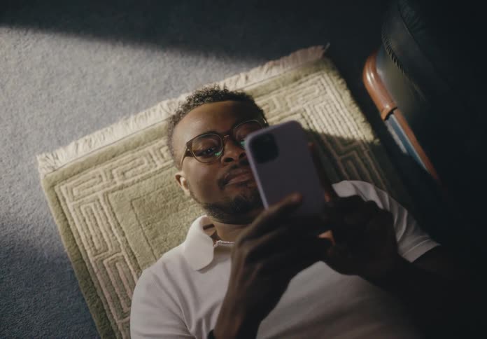 Man reclines on rug on floor while scrolling on smartphone